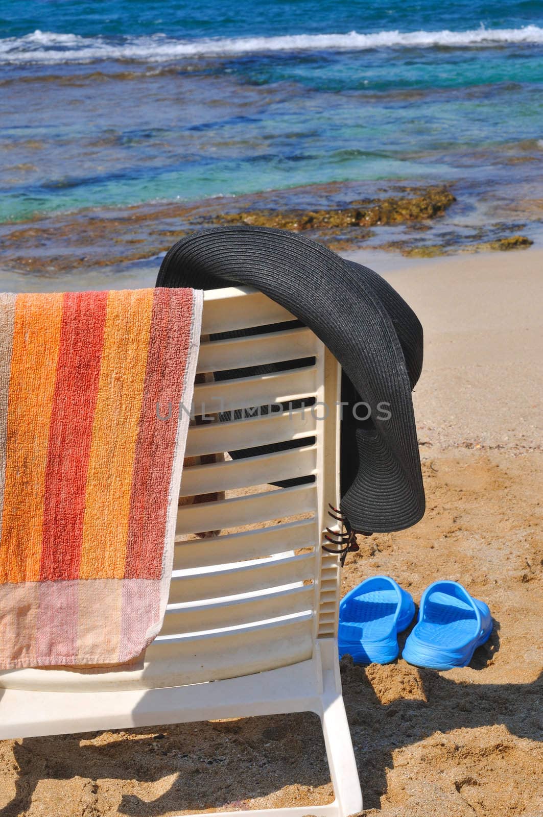 
A hat, a towel hanging on a chair on the beach by the sea