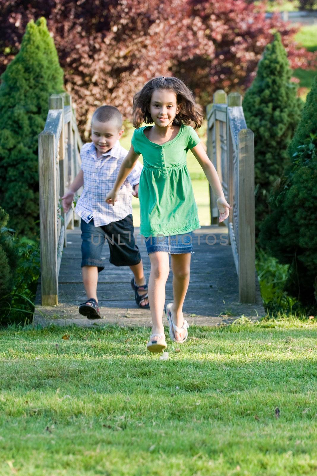 A cute little children running happily over a wooden bridge through the park.