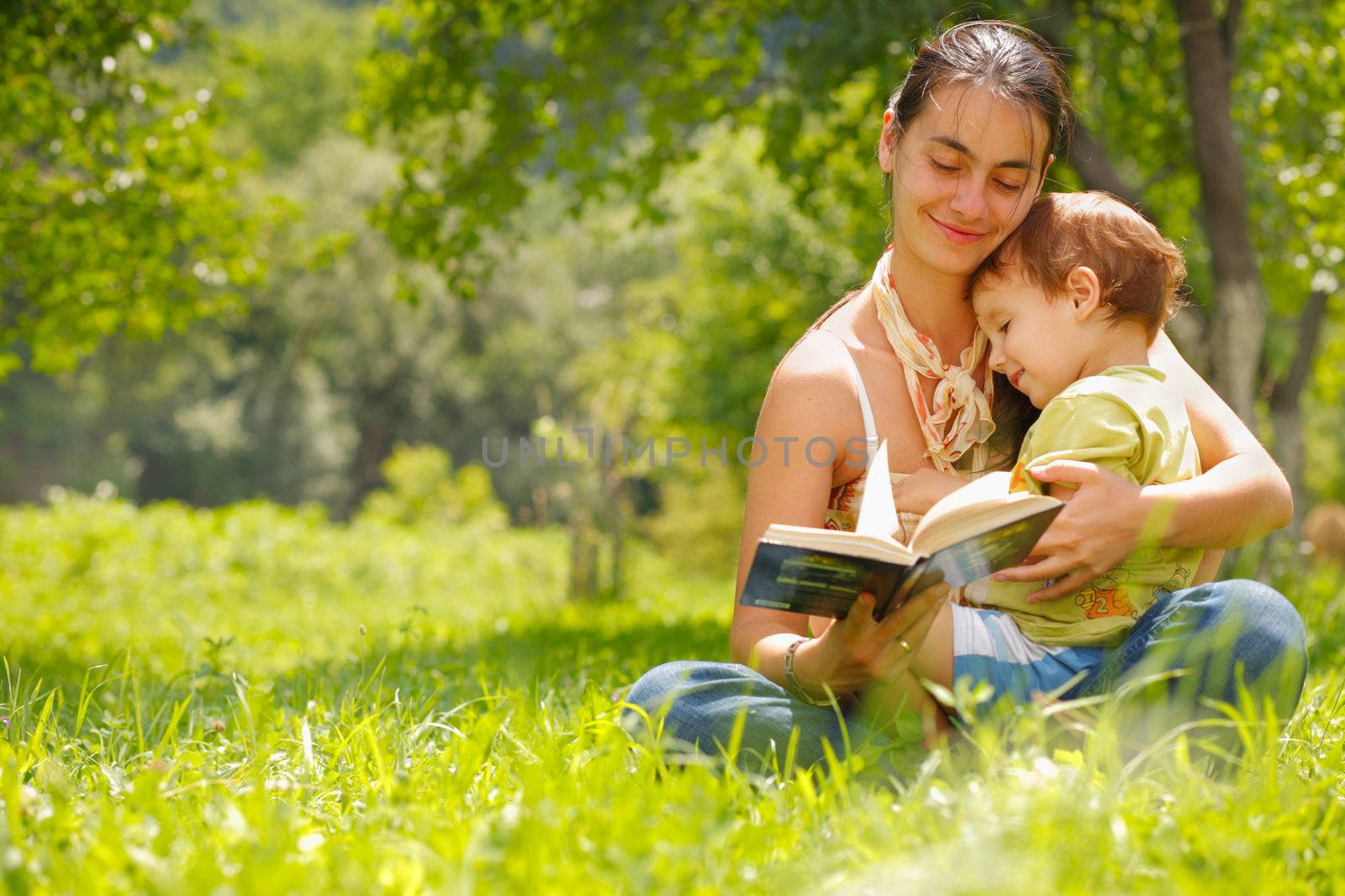 Happy mother and son reading a book outdoors by romanshyshak