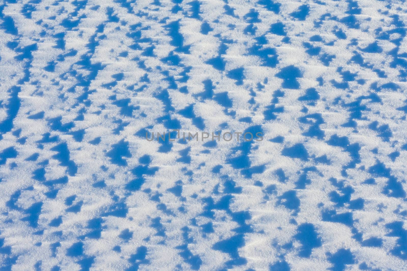 Windblown snow surface in bright sun, background texture pattern.