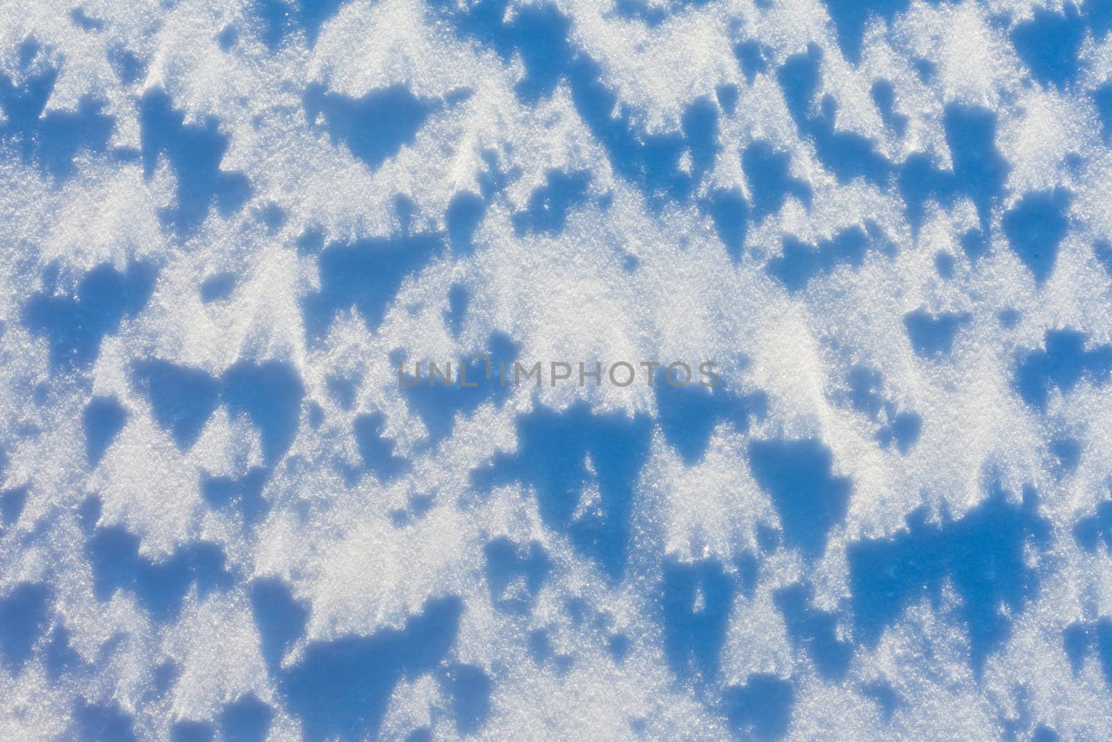 Windblown snow surface in bright sun, background texture pattern.