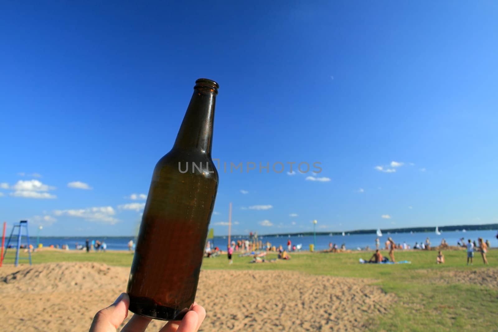 Bottle of beer against the beach, lake and blue sky
