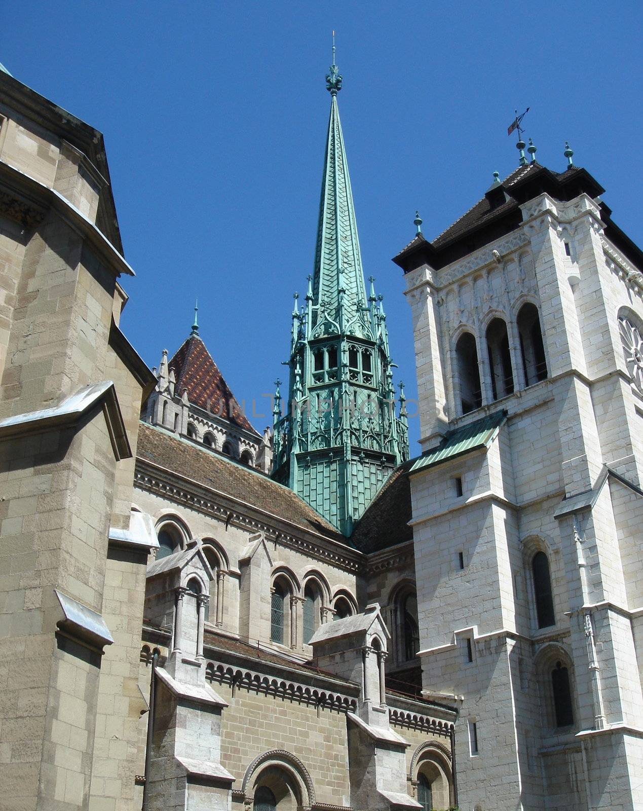 Green bell tower of a cathedral surrounded by other old buildings with deep blue sky