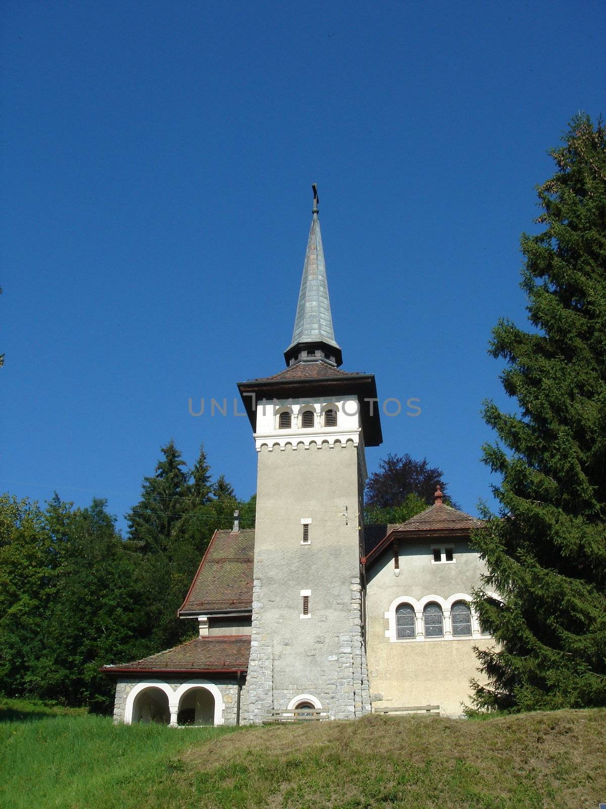 Small white church with tower among green vegetation with deep blue sky