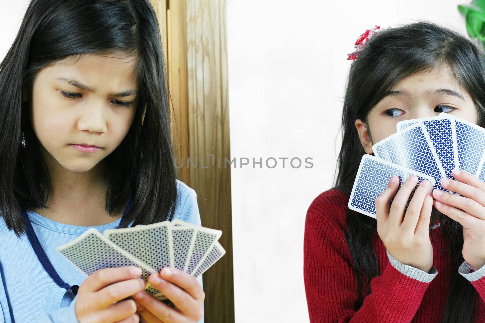 Two girls playing cards, one is cheating and looking at the other's hand