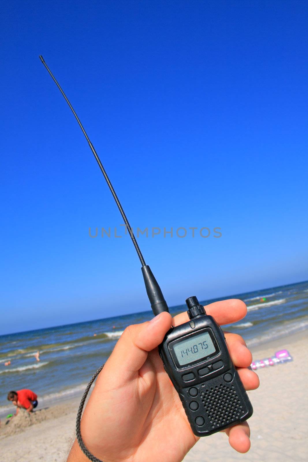 VHF transceiver in a hand against the beach and blue sky
