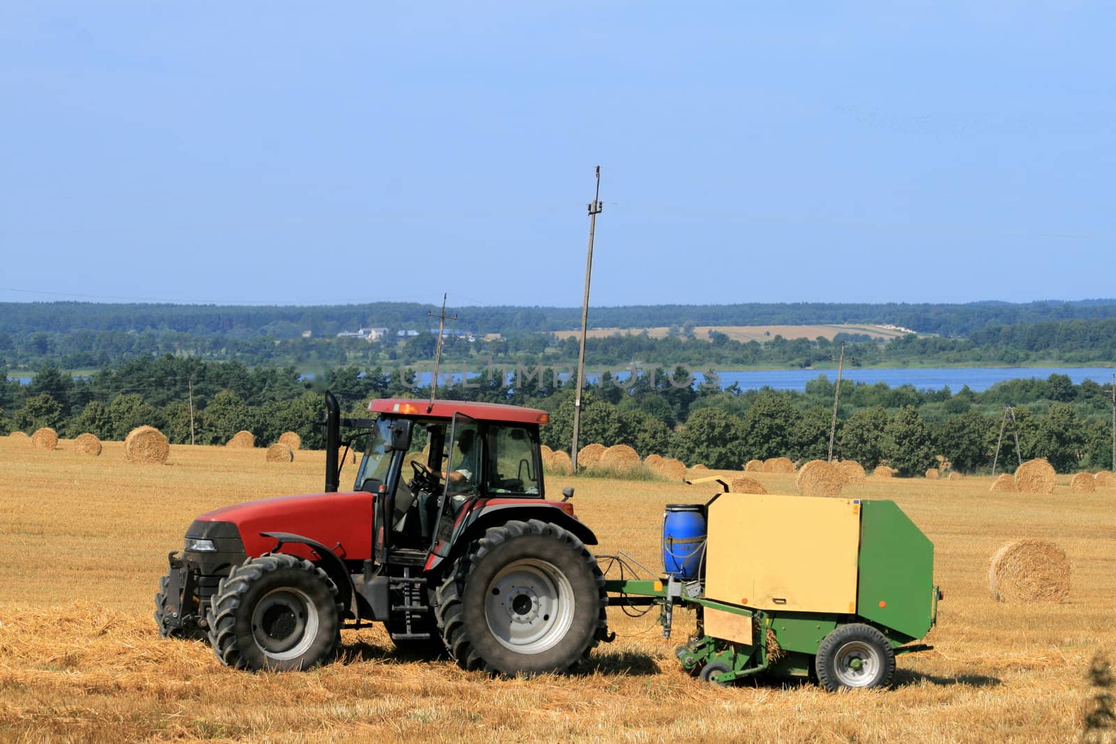 Landscape with tractor, straw bales and a lake
