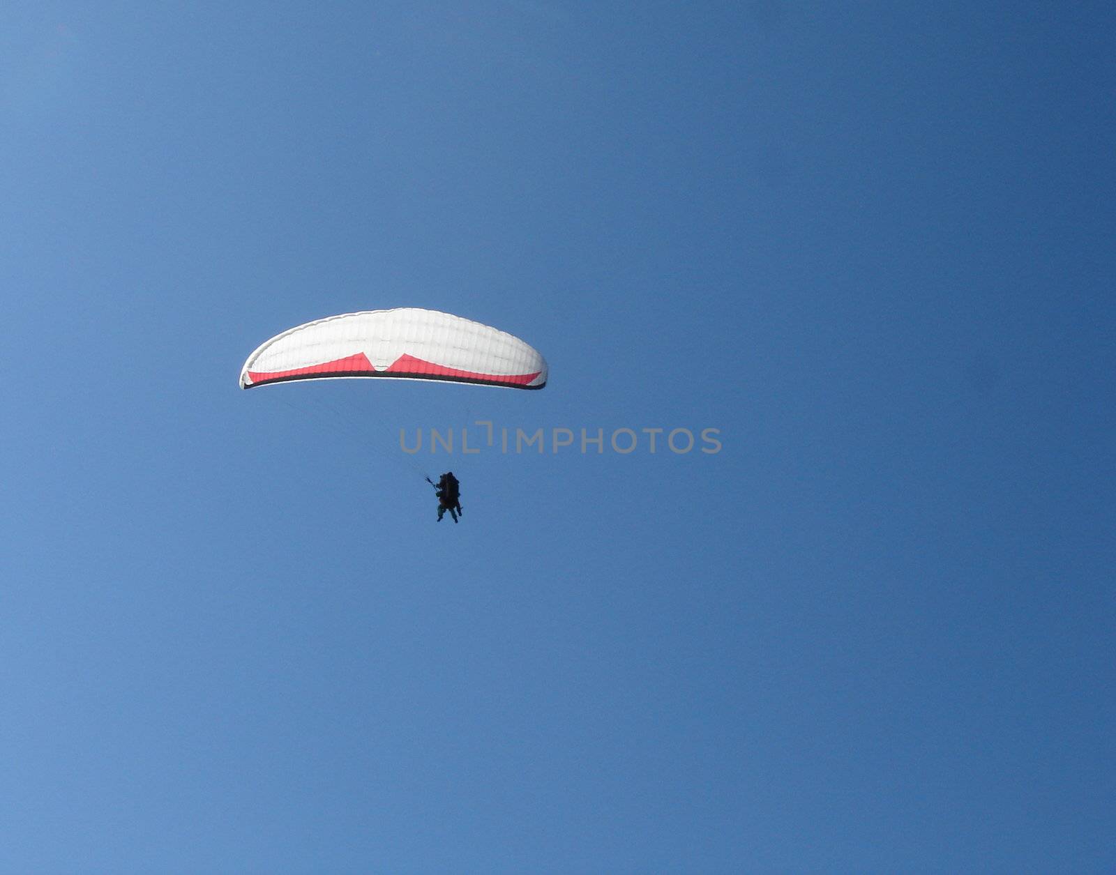 Small paragliders with white veil in deep blue sky