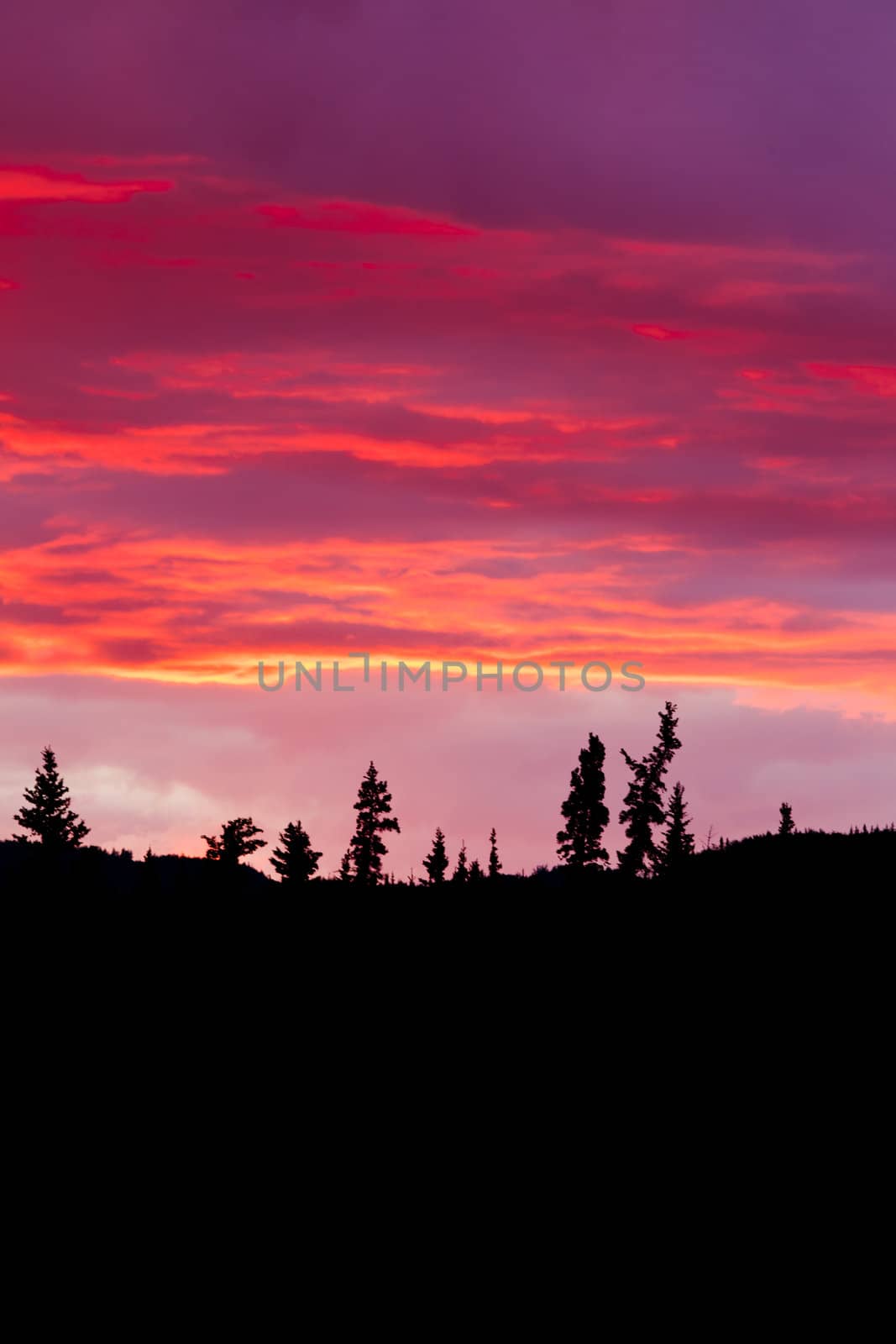 Cloudy sunset sky on fire over silhouette of forested hills.