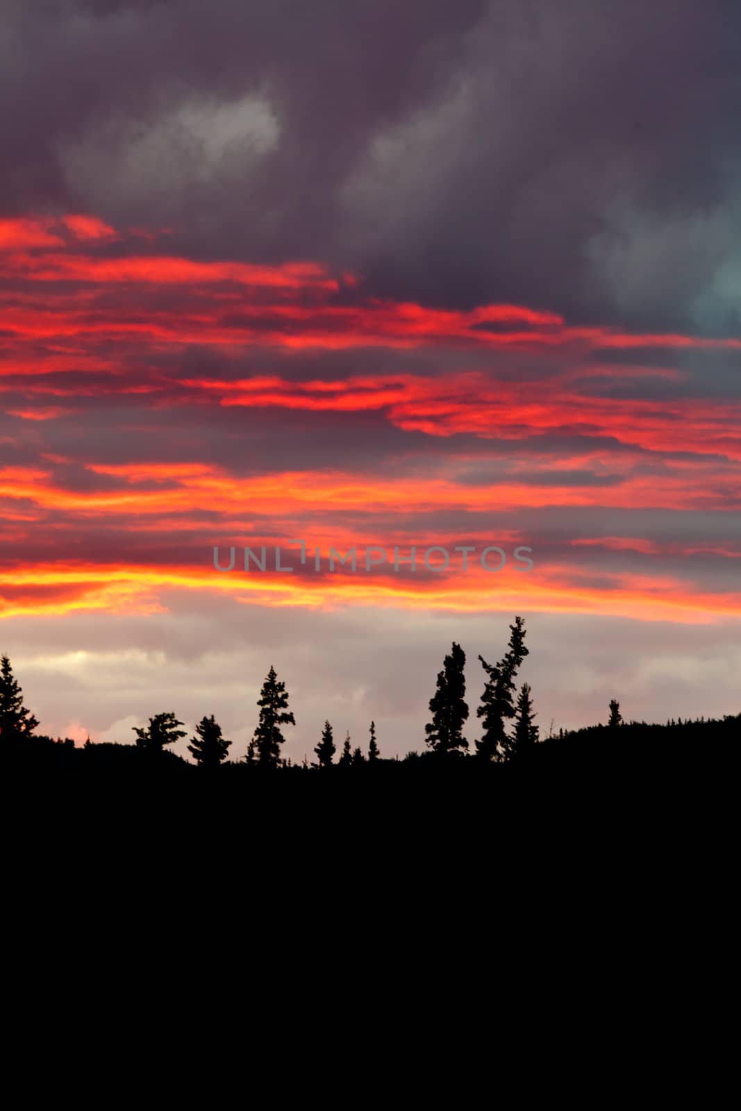 Cloudy sunset sky on fire over silhouette of forested hills.