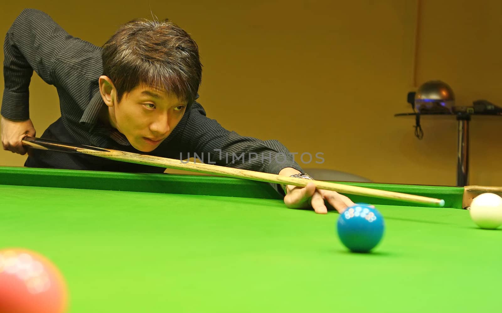 Young man concentrating while aiming at pool ball while playing billiards. 