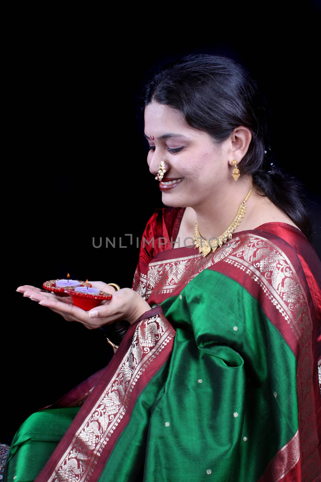 An Indian woman in a traditional green sari holding Oil-lamps on the occasion of Diwali festival, on black studio background.
