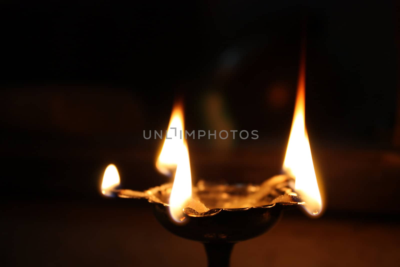 A traditional holy oil-lamp lit in a Hindu temple. The lamp is made of a long metal stem & floral bowl, with five places for wick / flames.