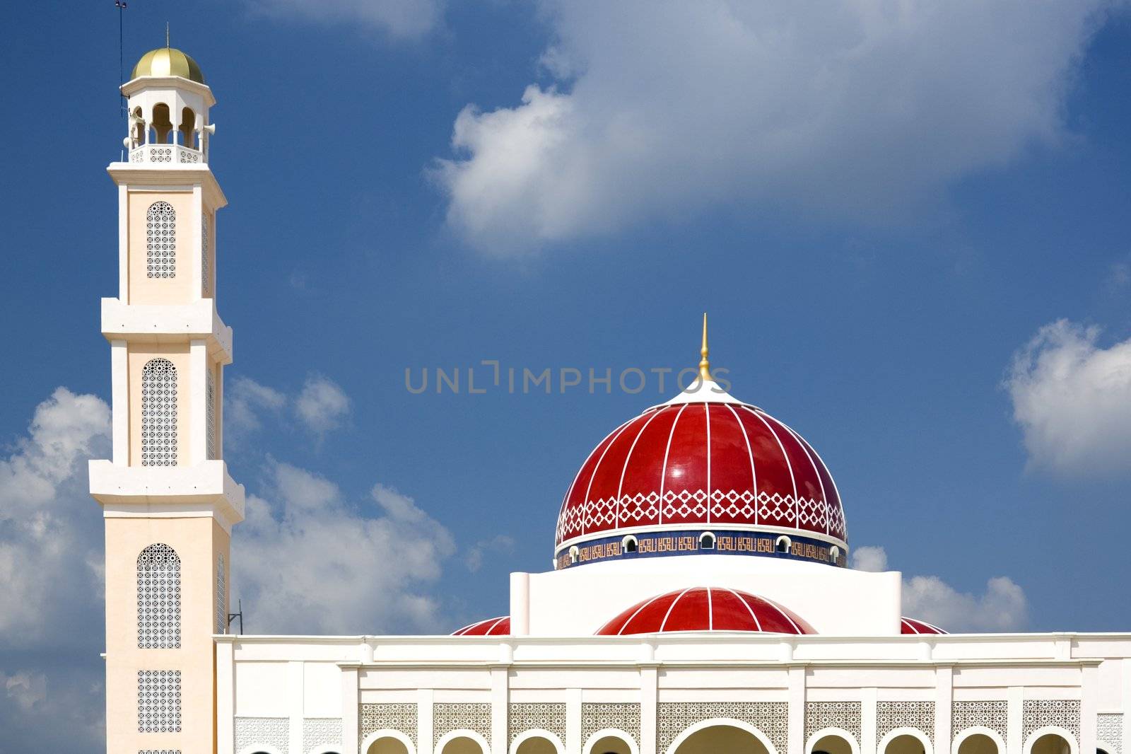 A modern red domed mosque in Malaysia against a backdrop of storm clouds.
