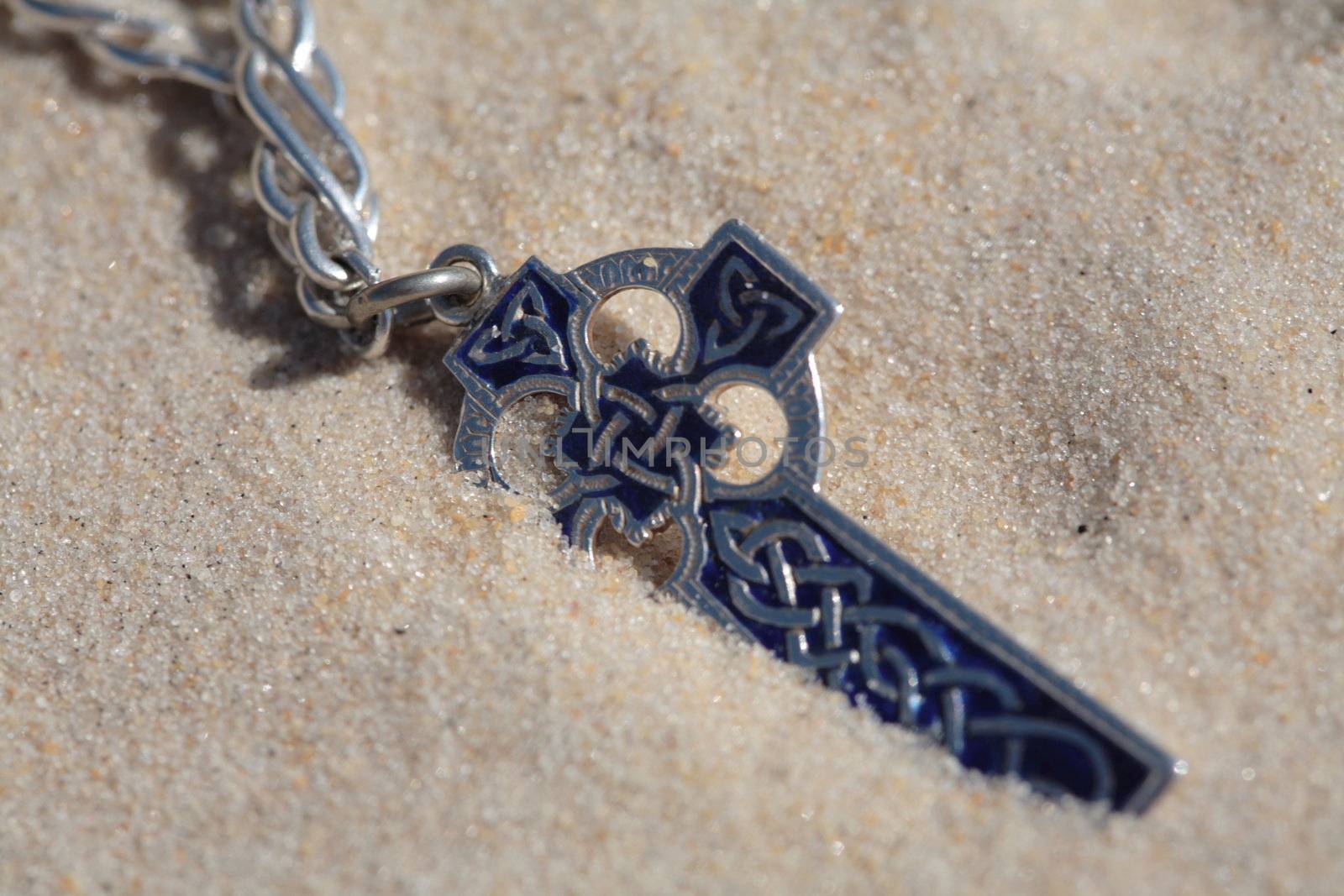 A silver and blue celtic cross on the sandy dunes.