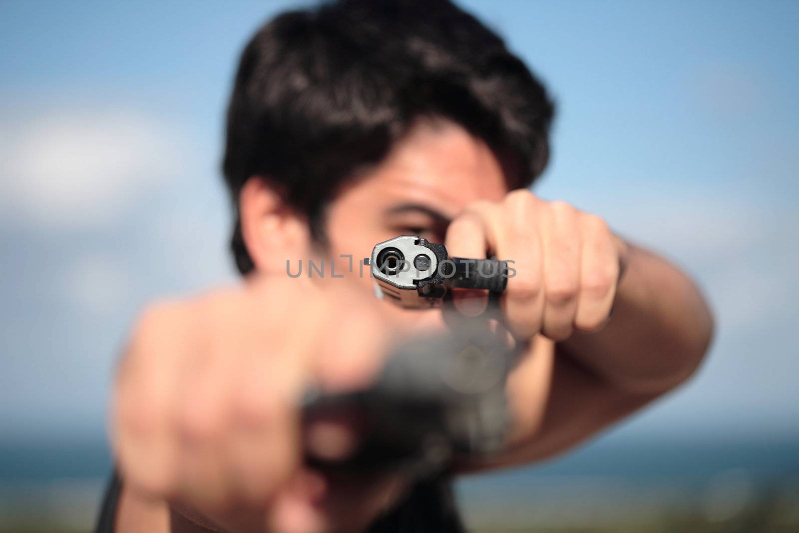 A young, robust man, in his 20's with dark hair pointing 2 pistols to the camera.