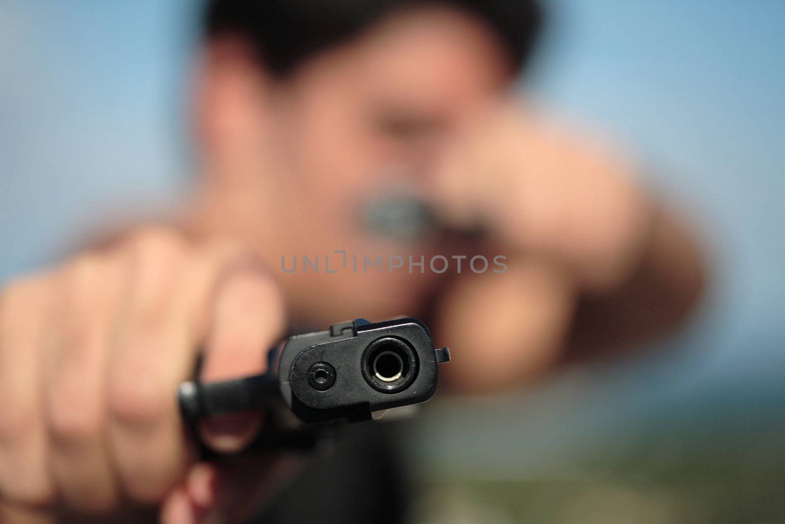 A young, robust man, in his 20's with dark hair pointing 2 pistols to the camera.