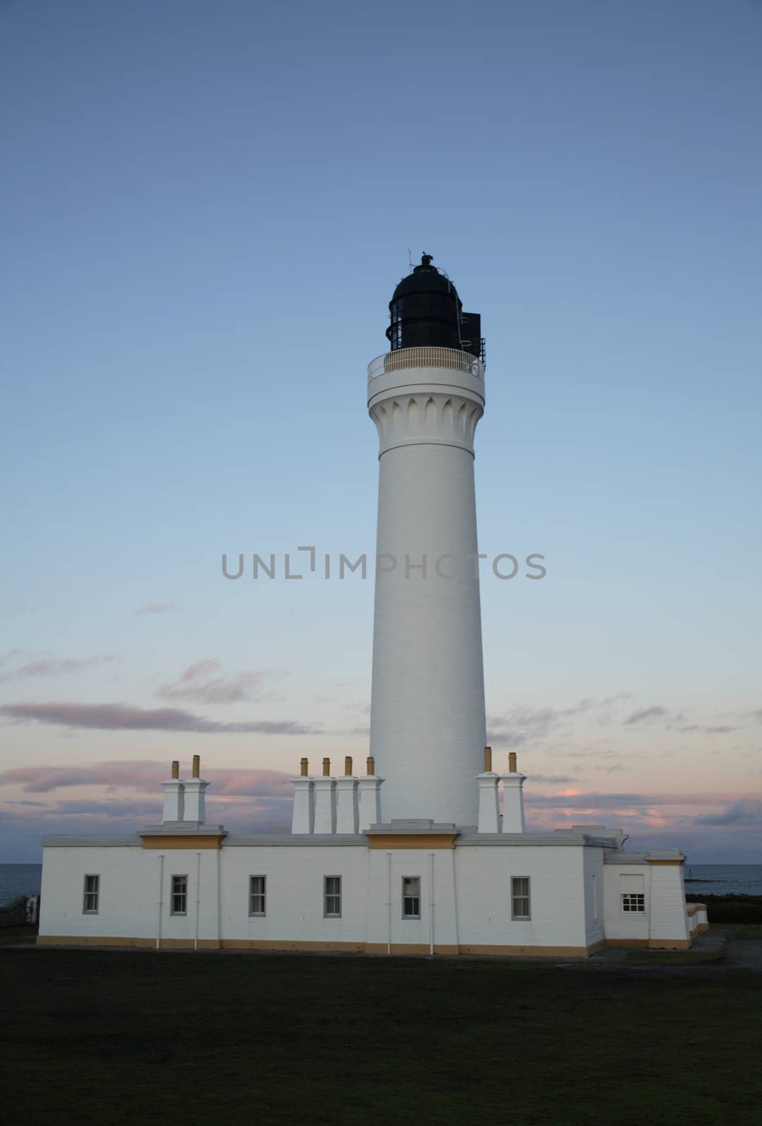 A white lighthouse at dusk and a blue sky.