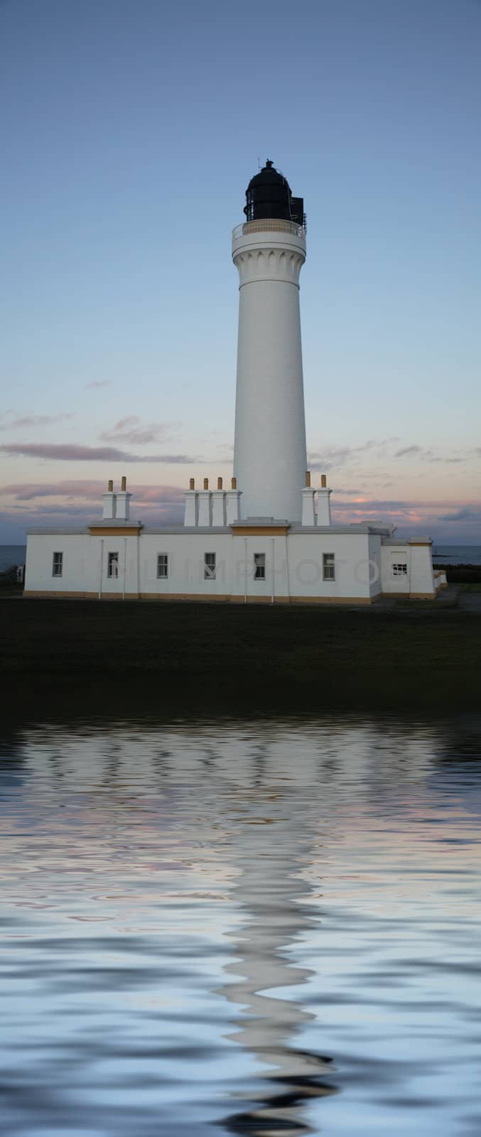 A white lighthouse at dusk and a blue sky.

(with water reflection)