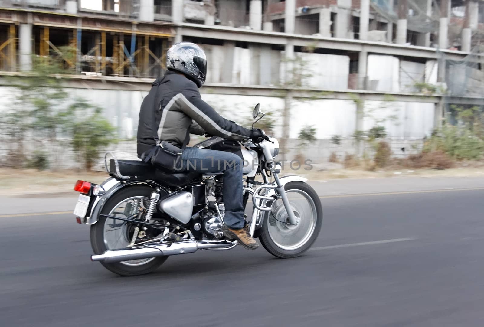 Motor biker breaks road rules by undertaking on the inside lane, horizontal landscape, copy space and crop space. Tarmac roads with white markings, derelict factory on roadside undergrowth