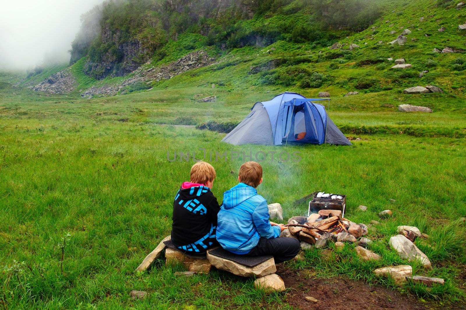 The fog is comming to a mountain camp. Two children at the campfire
