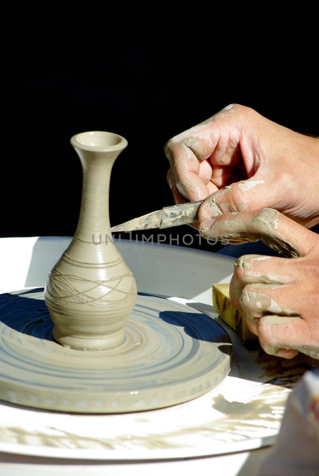 Potter's hands at work on decorating crude clay pot on the jigger