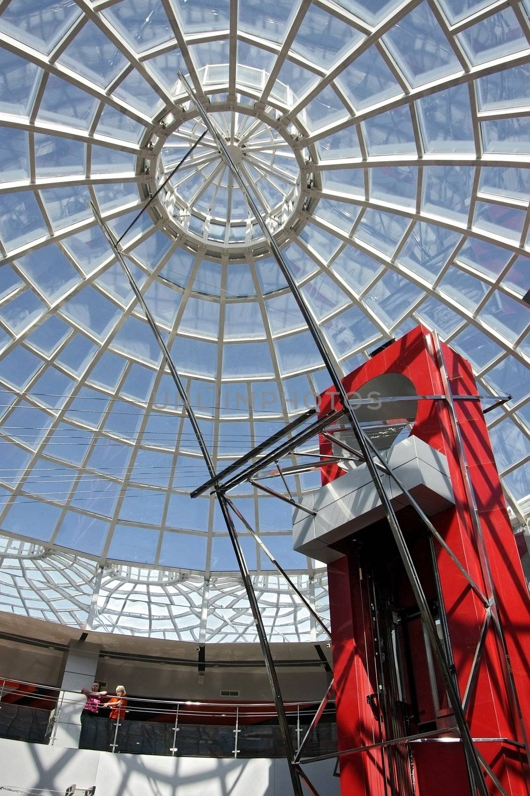 Huge hall of modern shopping centre with the glass lift and a transparent glass dome