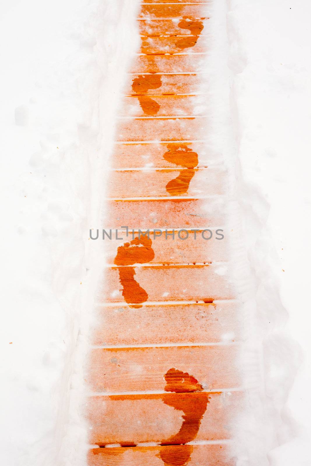 Barefooted human foot prints on frosted path on snow covered wooden deck planks (after sauna bath).