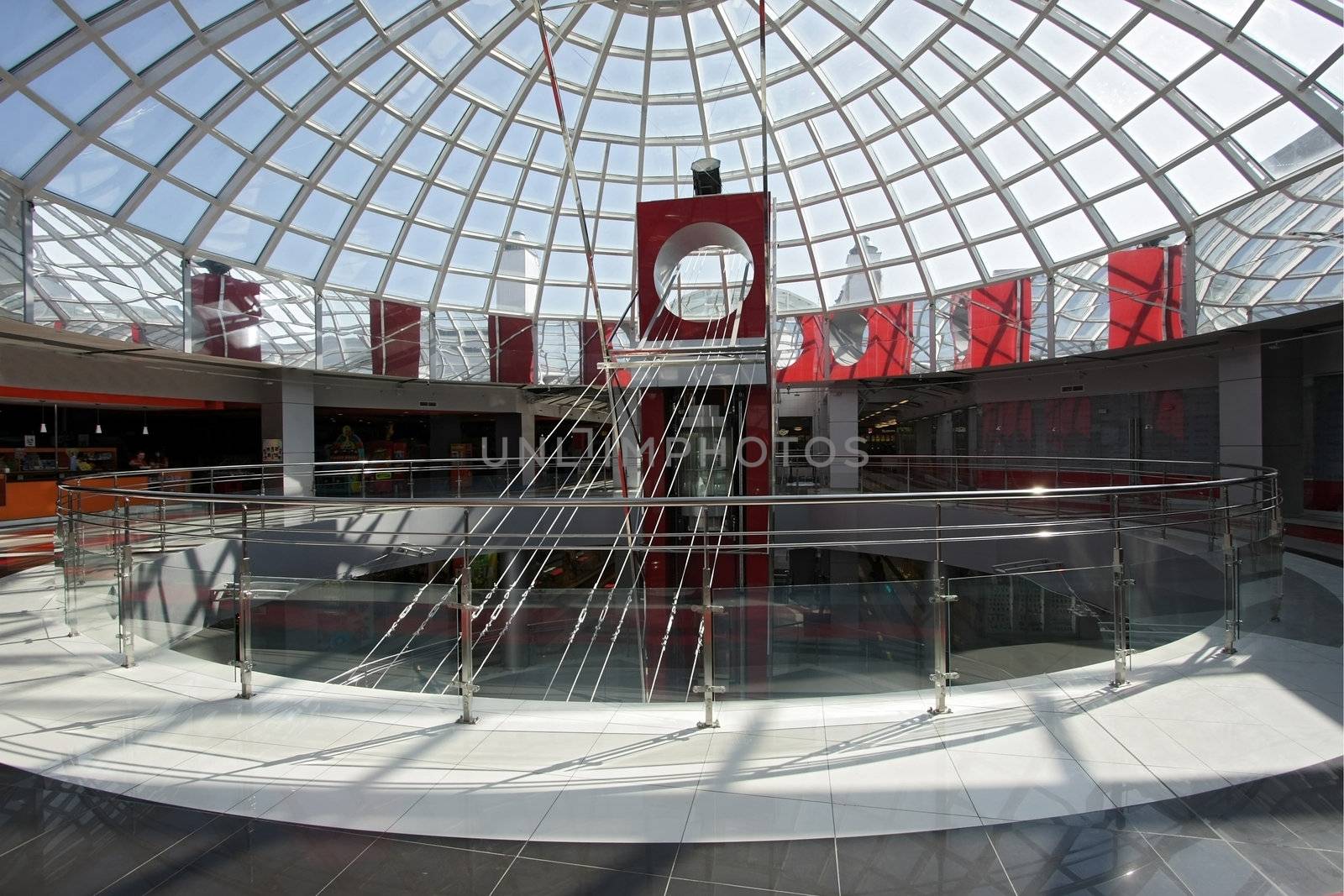 Huge hall of modern shopping centre with the glass lift and a transparent glass dome
