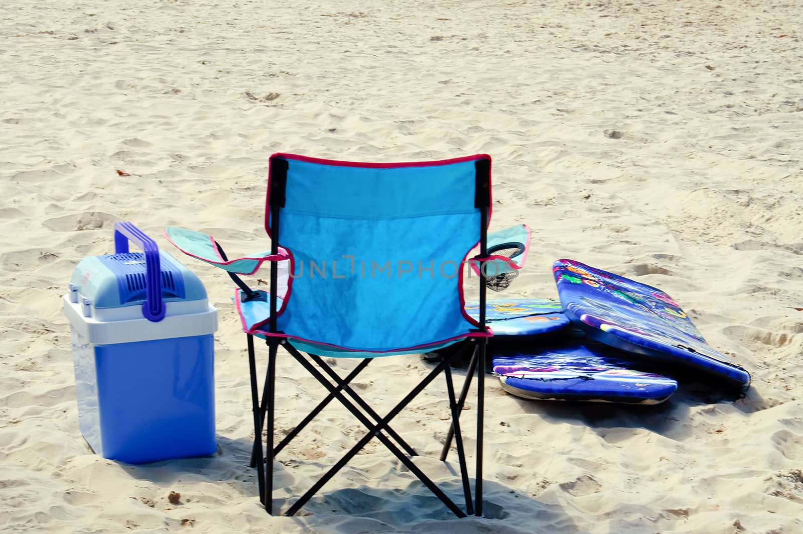 A blue nylon chair, cooler, and surf boards on a sandy beach