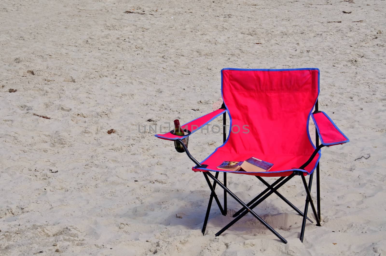A pink beach chair with a book and a bottle of wine
