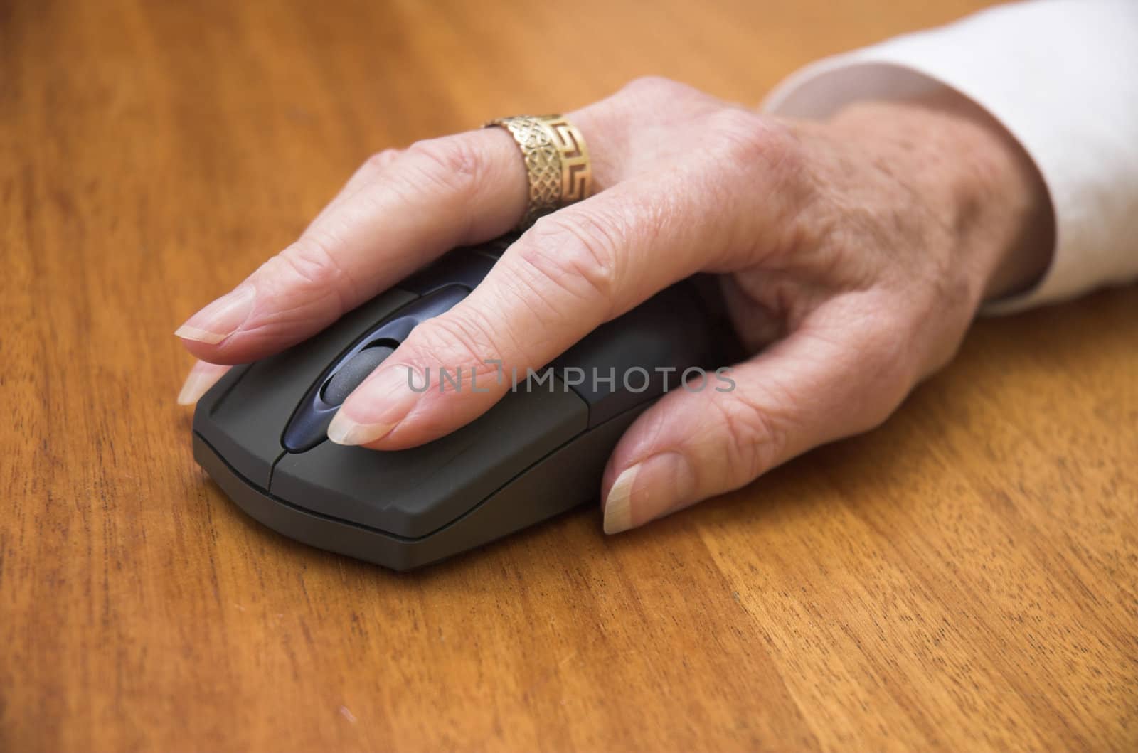 Older woman's hand using a wireless computer mouse. Focus is on the front of the mouse / end of the fingers.