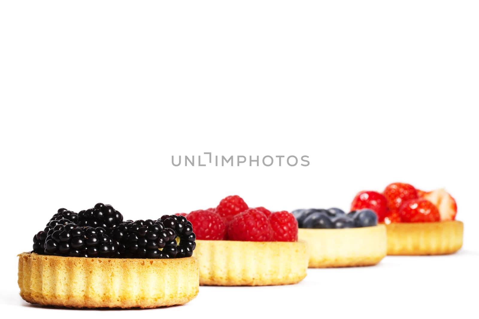 blackberries and other wild berries in tartlet cakes on white background