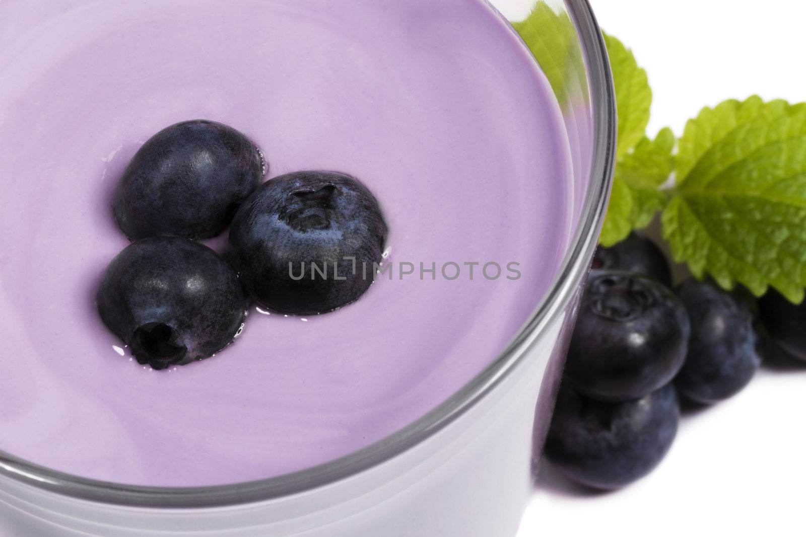 blueberries on top of a blueberry milkshake with blueberries and melissa aside on white background