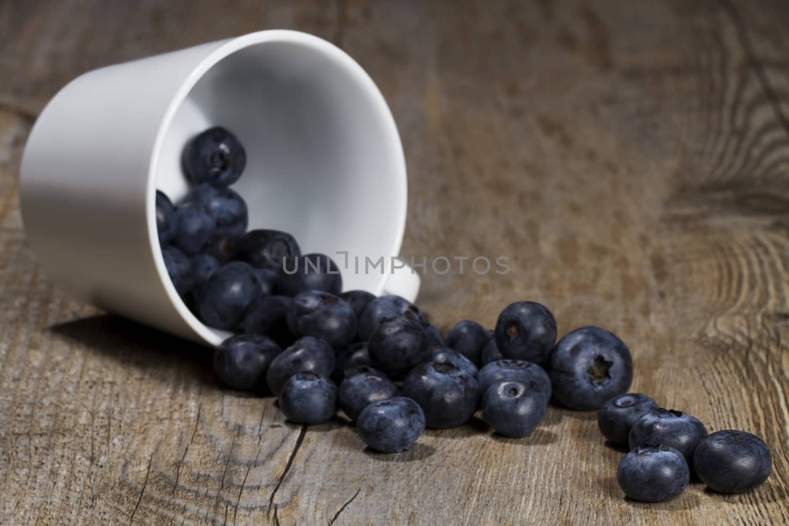blueberries rolling from a fell over cup on wooden background