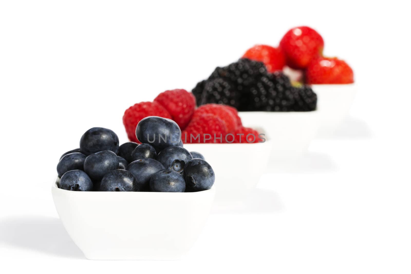 blueberries in a bowl with other wild berries in background on white background