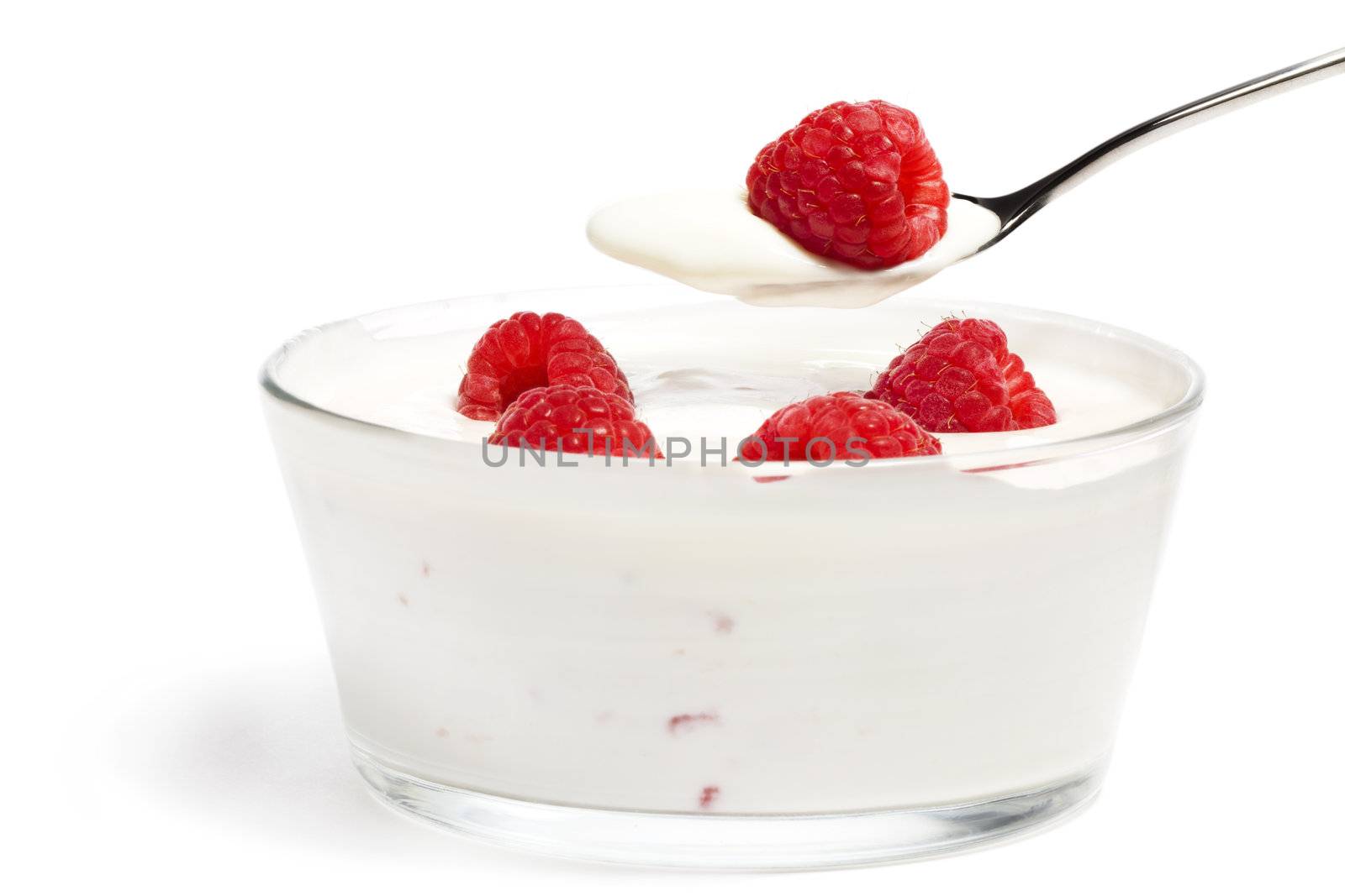 raspberry on a spoon over a dessert in a bowl with raspberries on white background