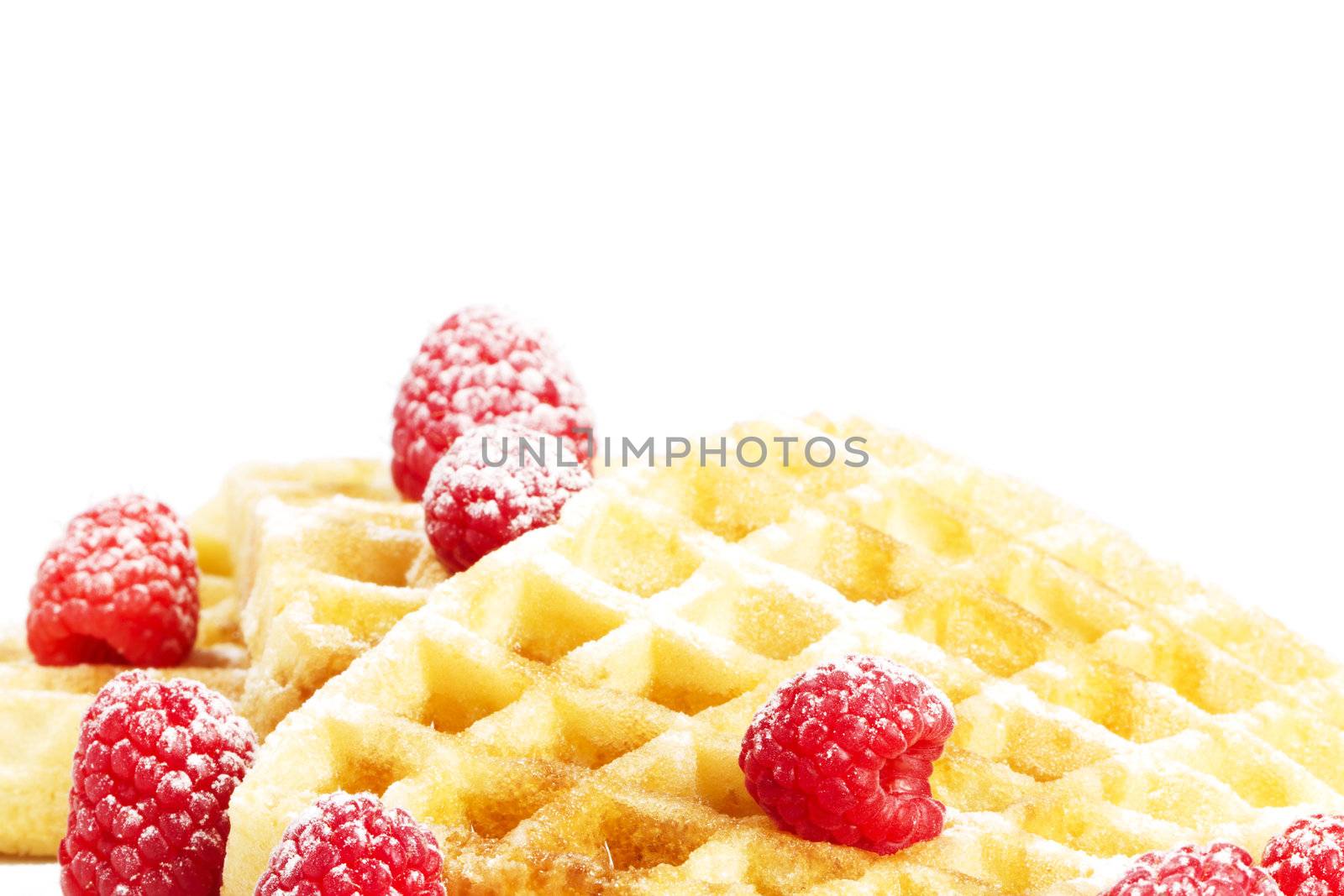 sugar covered raspberries on waffles with syrup on white background