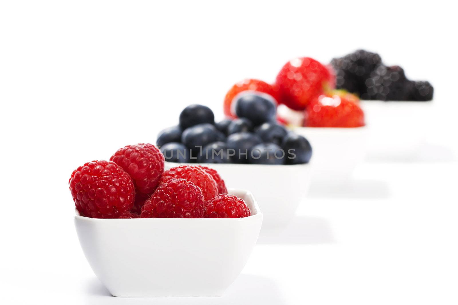 raspberries in front of wild berries in bowls on white background