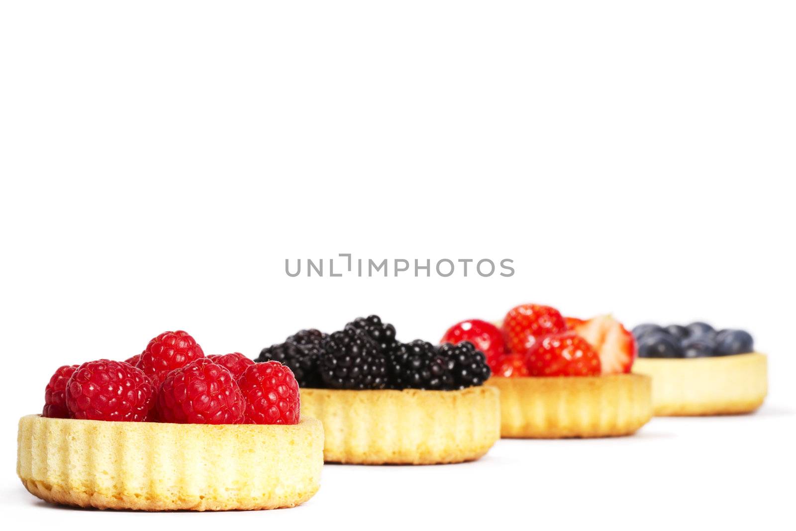raspberries in tartlet cake in front of other tartlet cakes with wild berries on white background