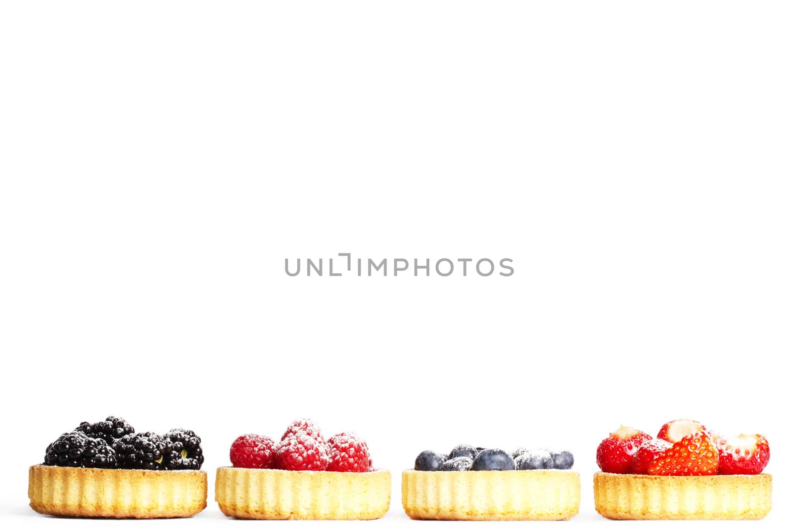 row of tartlets with sugar covered wild berries on white background