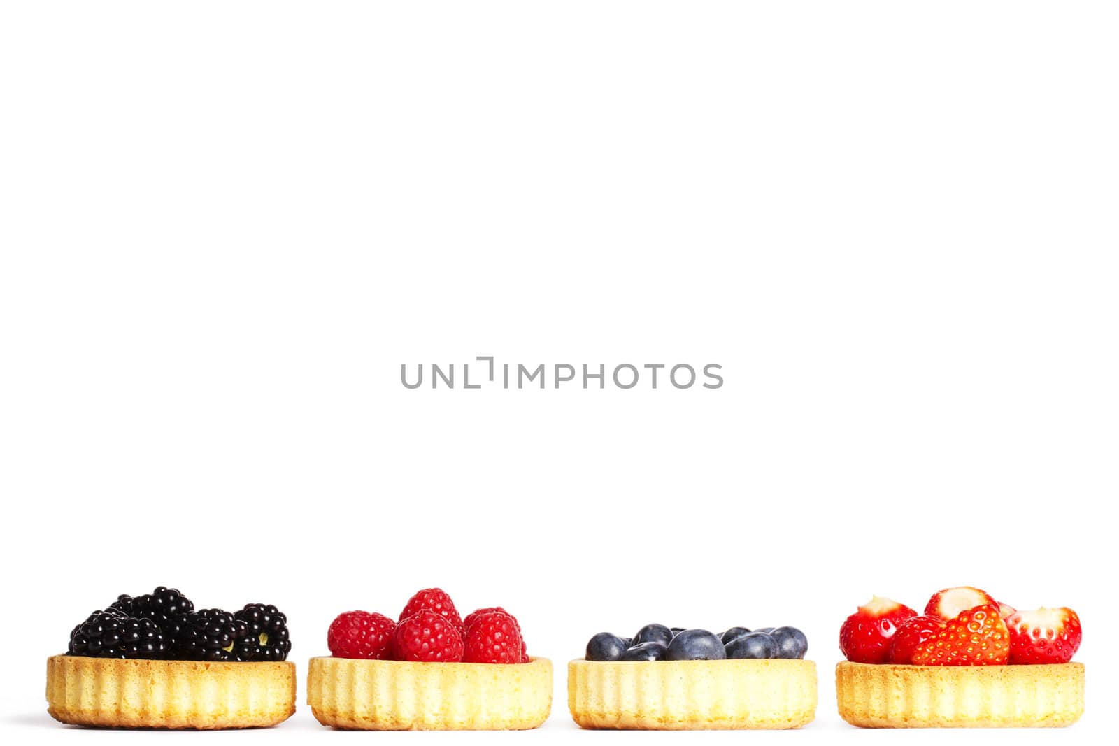 row of tartlets with wild berries on white background
