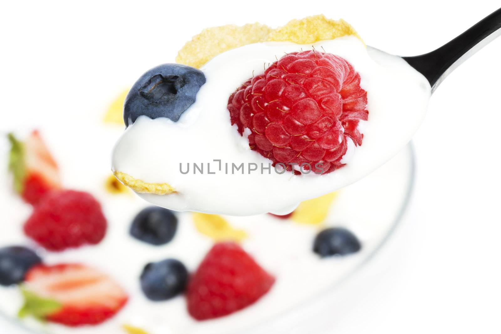 spoon with yogurt blueberry and a raspberry and cornflakes over a dessert on white background