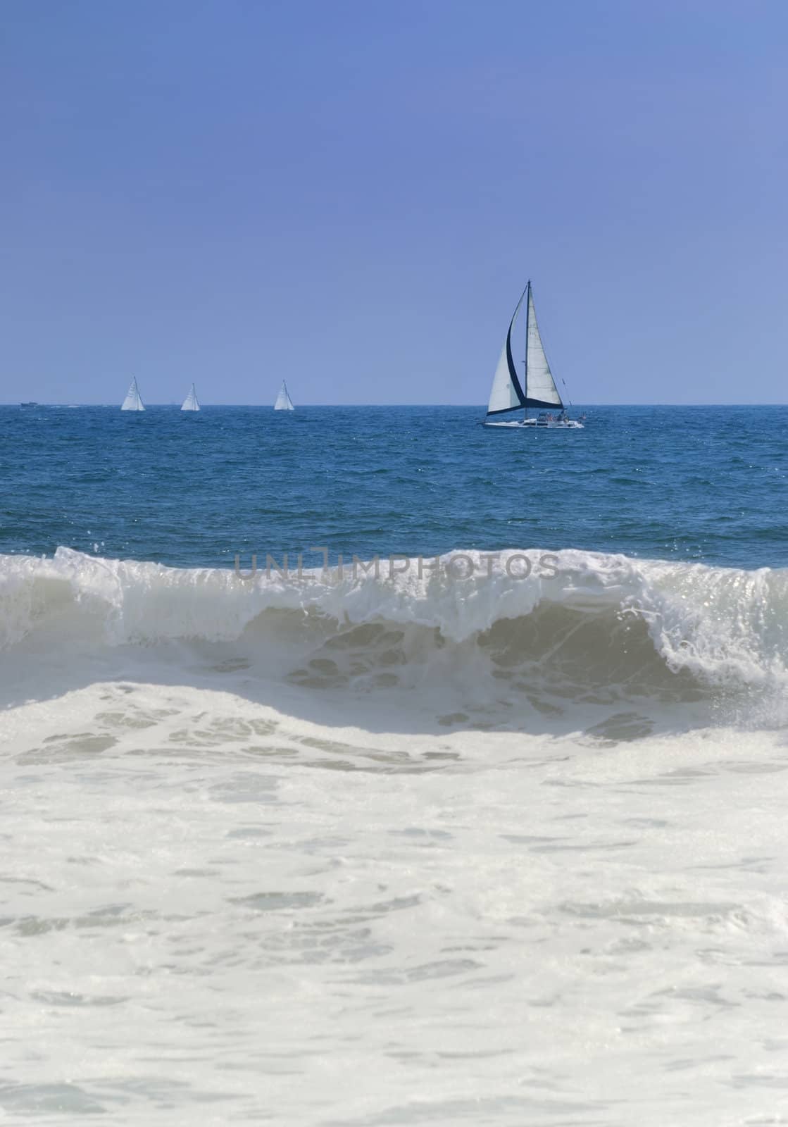 Sail boats at sea with crashing wave in foreground.