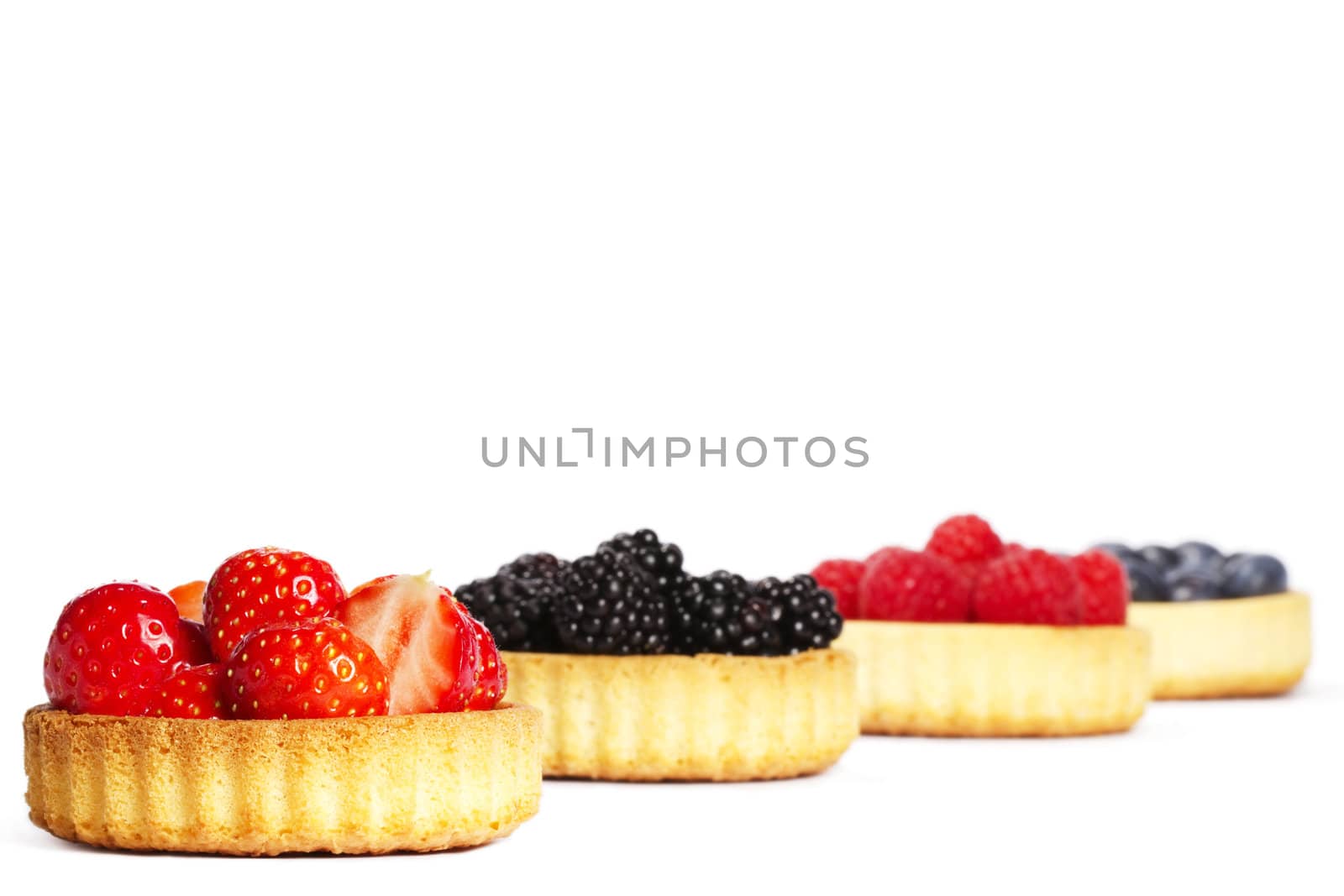 strawberries in a tartlet in front of wild berries in tartlets on white background