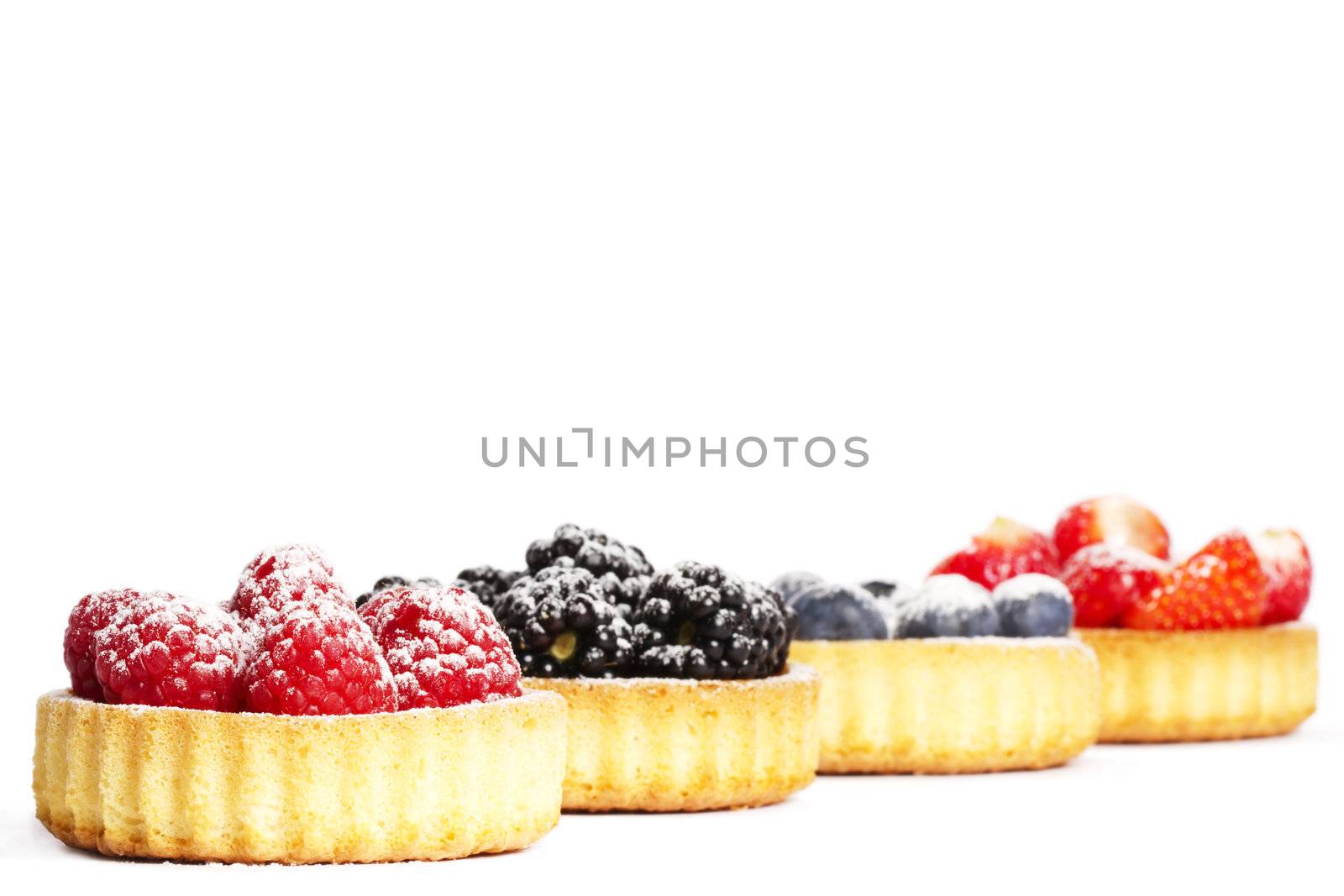 sugar covered raspberries in a tartlet in front of wild berries on white background