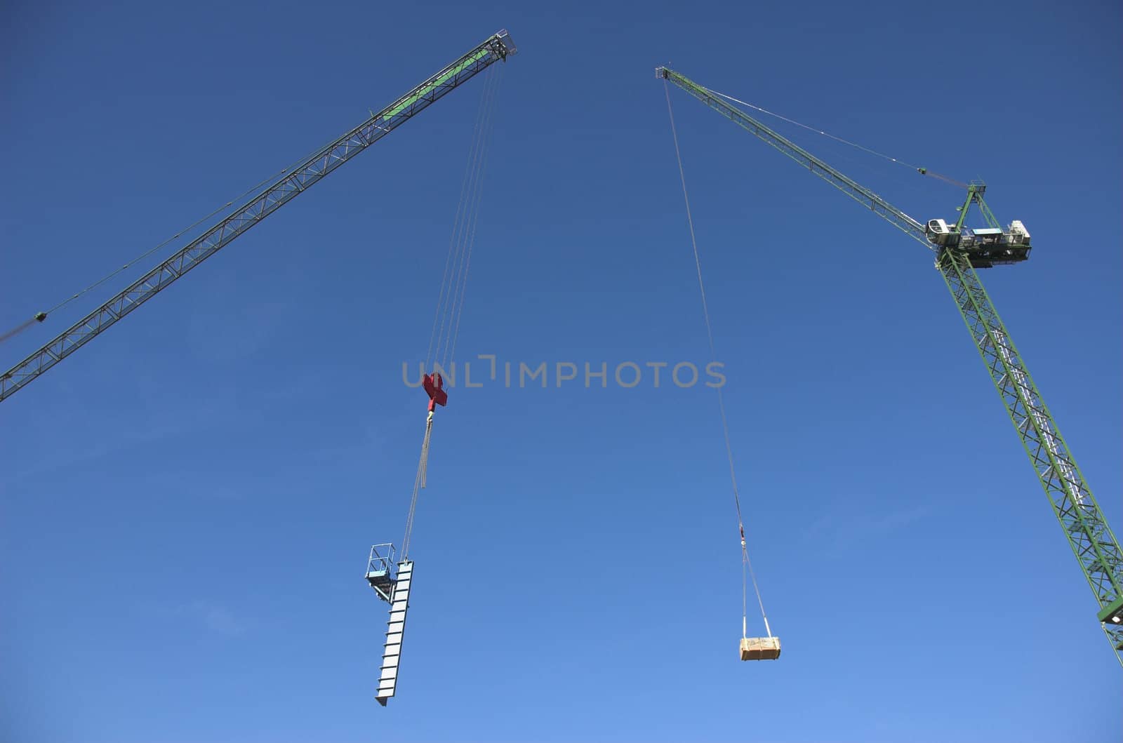 Construction cranes tower in the sky as they move equipment and materials around a construction site..