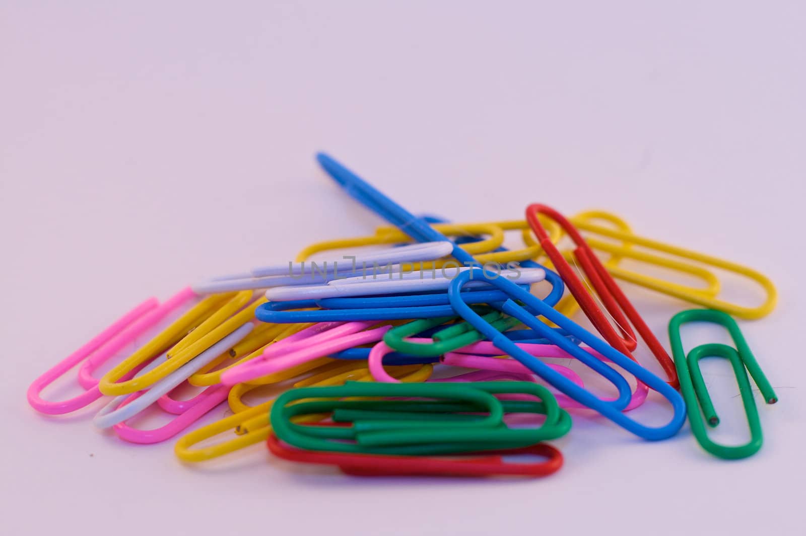 A pile of brightly colored paper clips over white