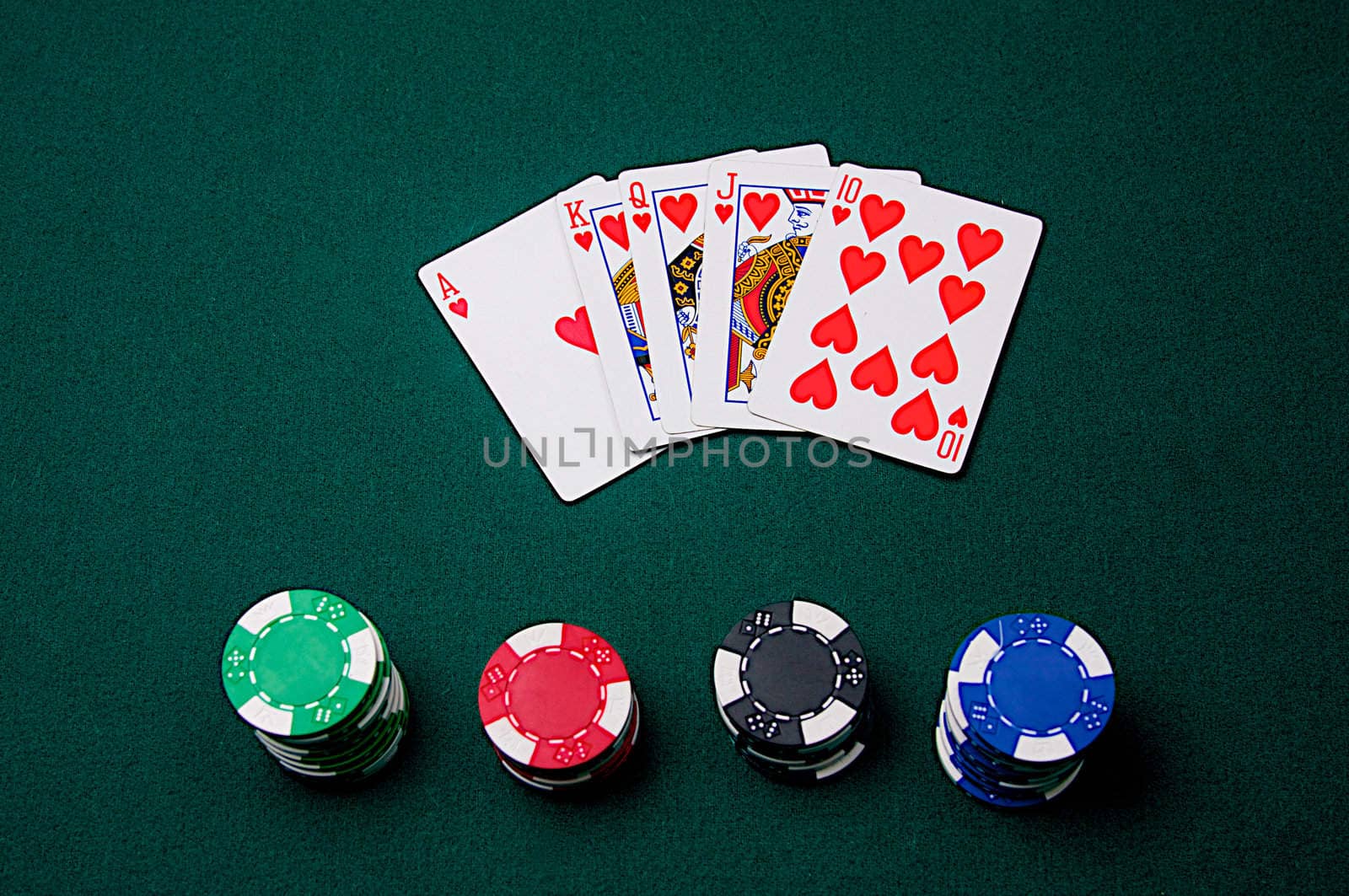 A royal flush is laid out with poker chips on green felt