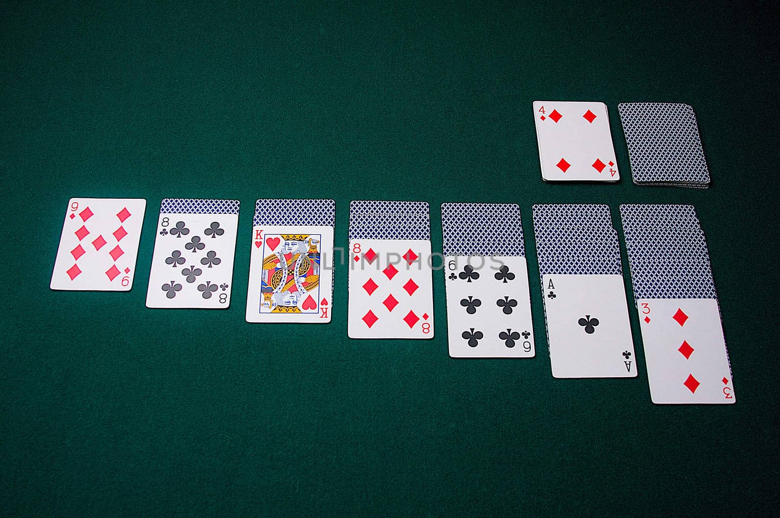 Playing cards are set up for a game of klondike solitaire, on green felt.